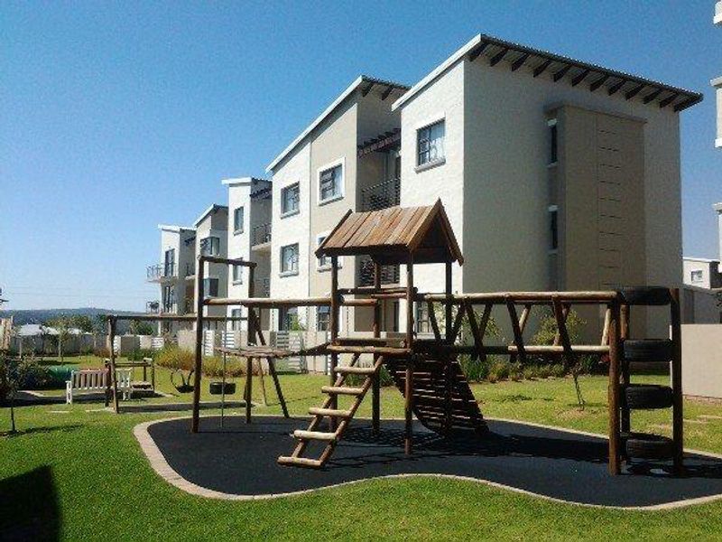 A well-maintained communal garden area featuring a wooden playground structure set against the backdrop of a modern multi-story apartment complex.
