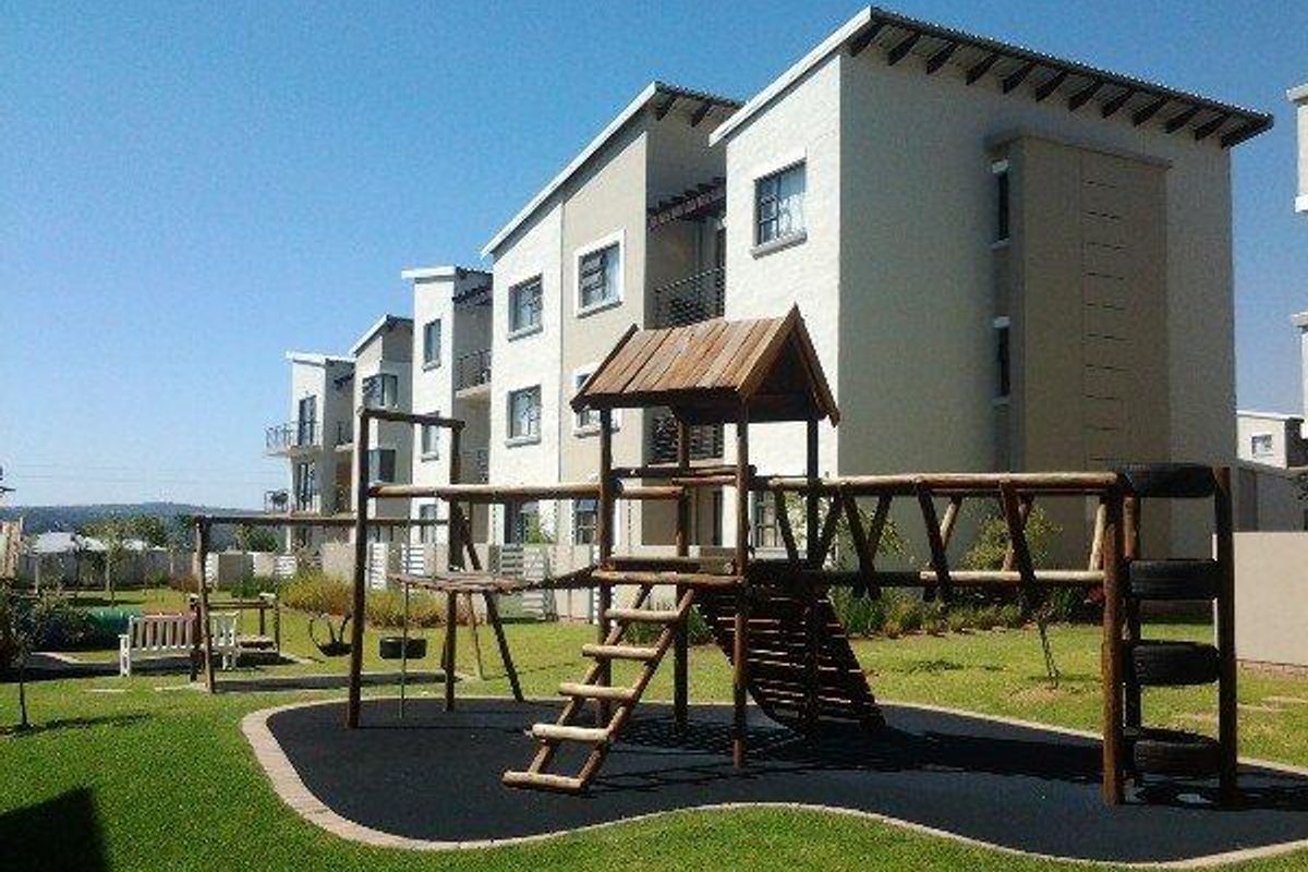 A well-maintained communal garden area featuring a wooden playground structure set against the backdrop of a modern multi-story apartment complex.