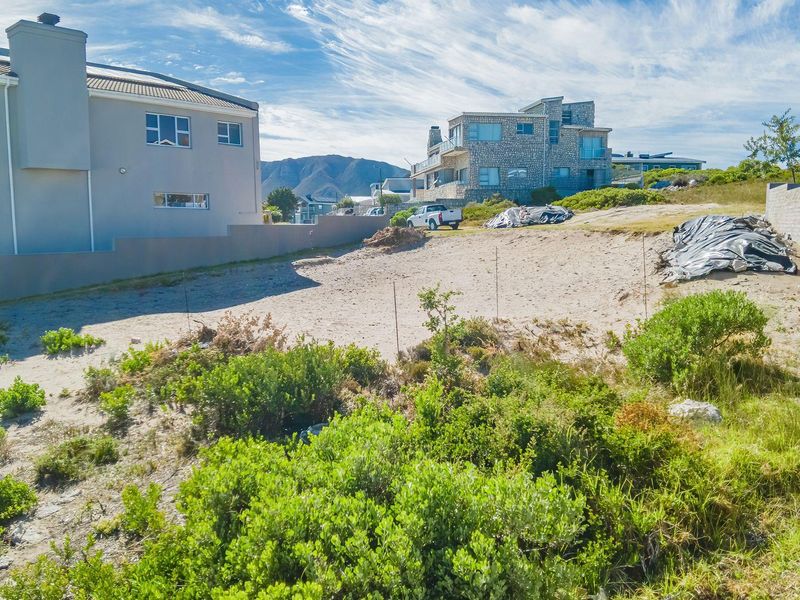 A vacant residential plot featuring sandy terrain, enclosed by boundary walls, situated in a developed neighborhood with surrounding residential properties.