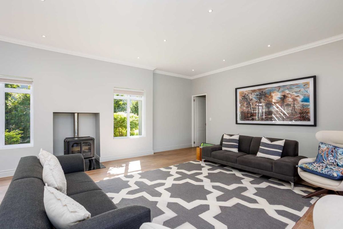 A bright and spacious living room featuring timber flooring, recessed downlights, and a built-in wood-burning stove.