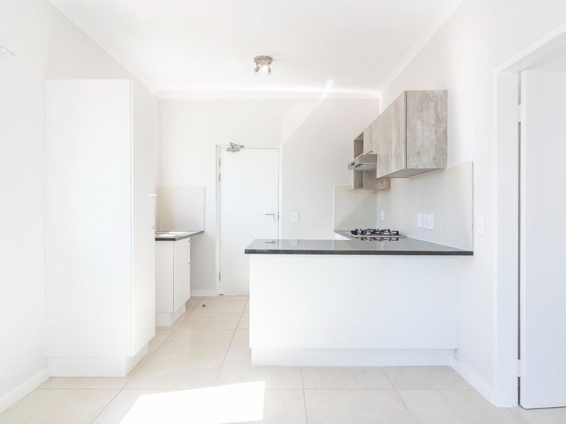 A clean, modern kitchen featuring white cabinetry, stone countertops, a gas hob with extractor fan, and neutral tiled flooring in an open-plan layout.
