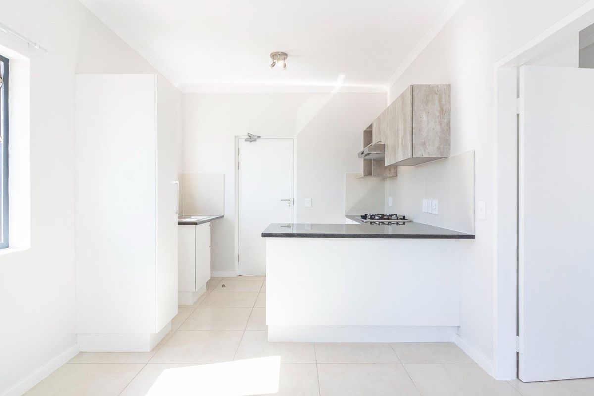A clean, modern kitchen featuring white cabinetry, stone countertops, a gas hob with extractor fan, and neutral tiled flooring in an open-plan layout.