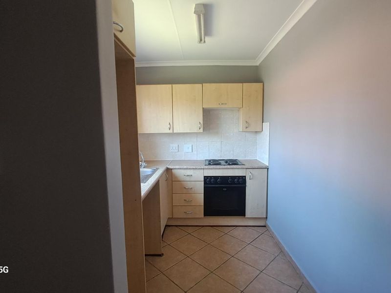 A compact kitchen featuring light wood-finish cabinetry, built-in oven and hob, tiled backsplash, and ceramic floor tiles.