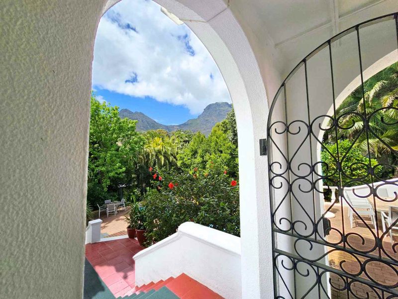 A view from an arched doorway looking out over a lush garden and mountain landscape, featuring a decorative wrought iron gate and tiled stairs.