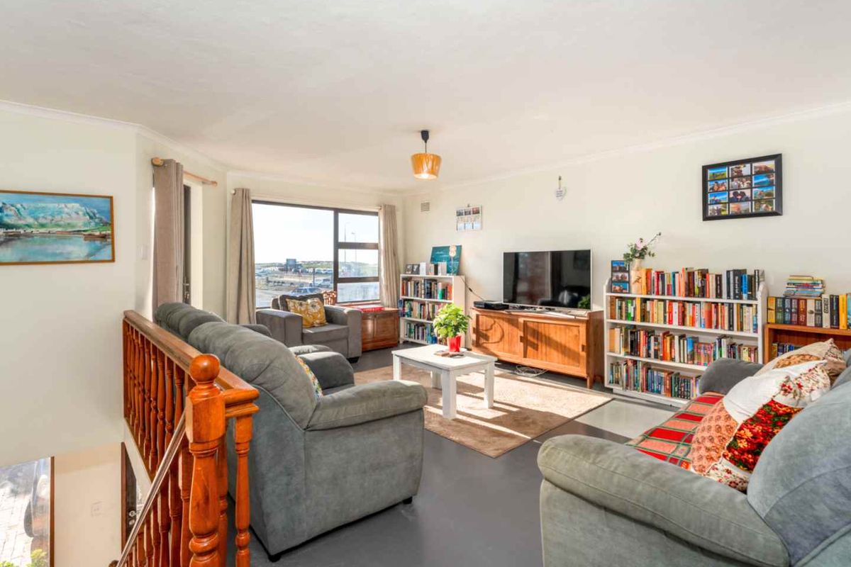 A bright and spacious living room featuring large windows, a wooden staircase railing, and neutral flooring, offering a comfortable and inviting atmosphere.