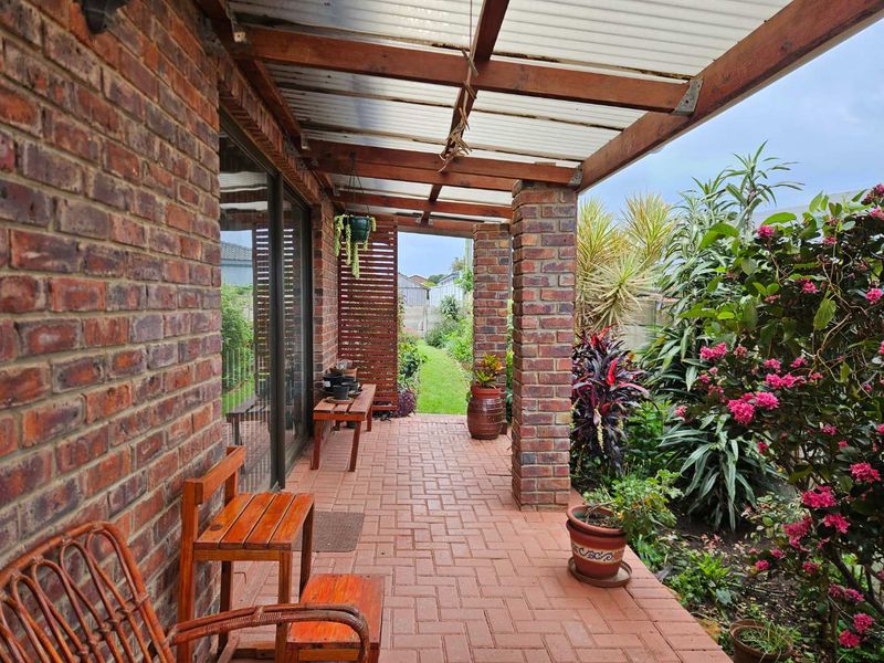 A covered outdoor patio featuring brick paving, sturdy brick pillars, and timber rafters, providing a seamless transition to the rear garden area.