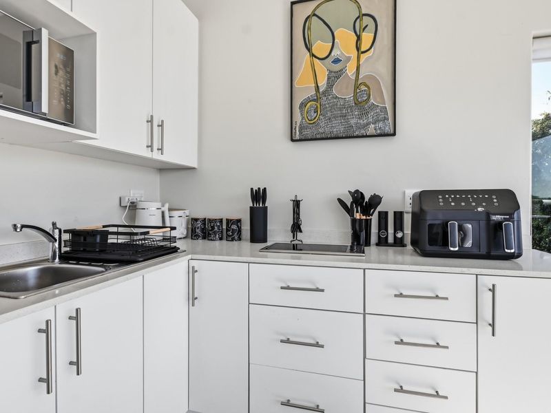 A modern, compact kitchen featuring white cabinetry, quartz countertops, a built-in microwave, and an integrated induction hob.