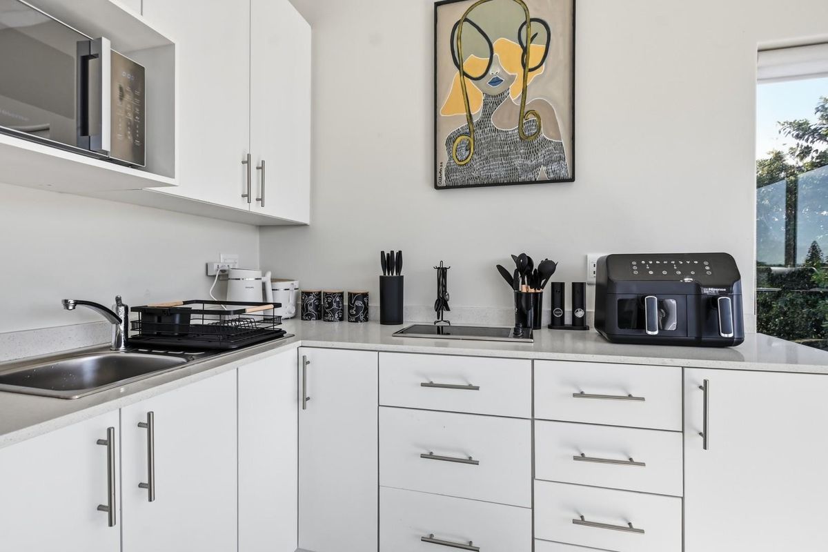 A modern, compact kitchen featuring white cabinetry, quartz countertops, a built-in microwave, and an integrated induction hob.