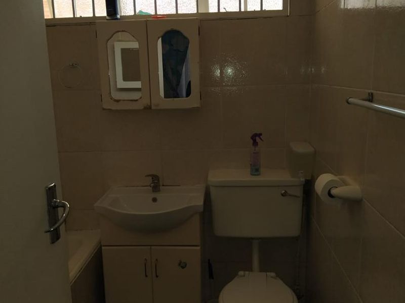 A compact bathroom featuring a vanity basin, toilet, and tiled finishes. The space requires cosmetic updates and floor tile repairs.