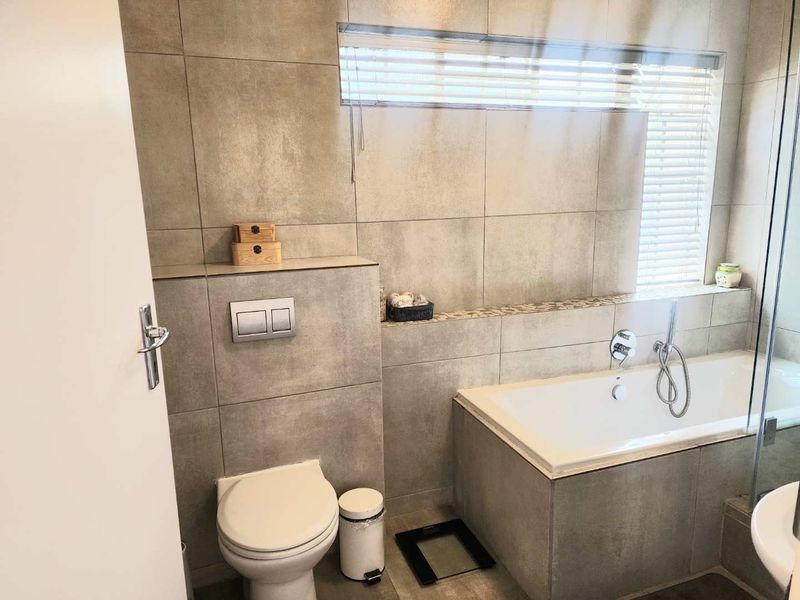 Modern bathroom featuring large-format grey wall tiles, a built-in bathtub, and a wall-mounted toilet with a concealed cistern.
