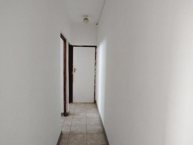 A narrow, empty hallway featuring tiled flooring and plain white walls, providing access to adjacent rooms within the cottage.
