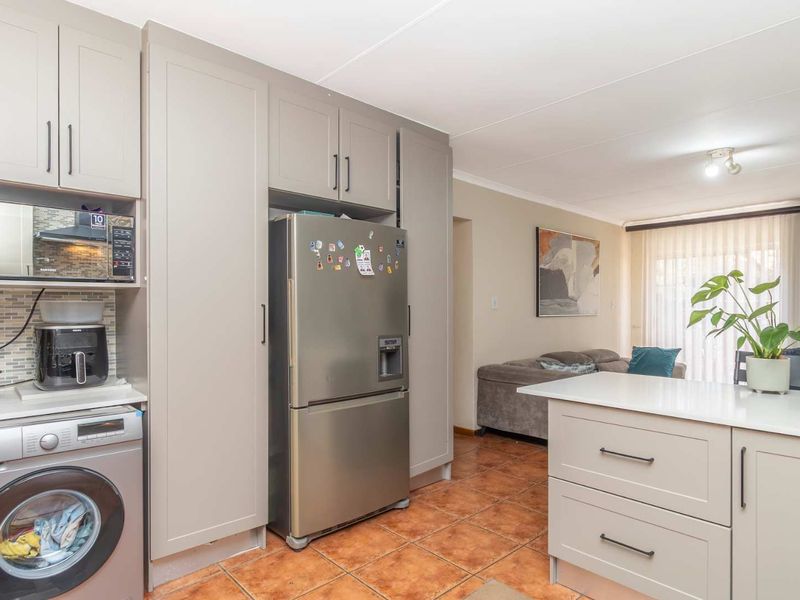 Open-plan kitchen and living area featuring modern grey cabinetry, a central island with stone countertop, and tiled flooring throughout.