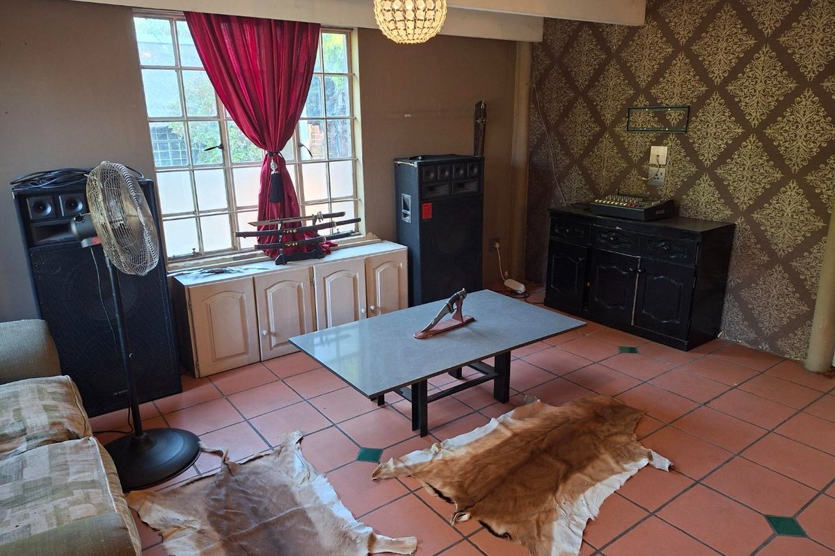 A living room featuring terracotta tiled flooring, exposed ceiling beams, and a lattice window, offering a dated aesthetic ready for modernization.