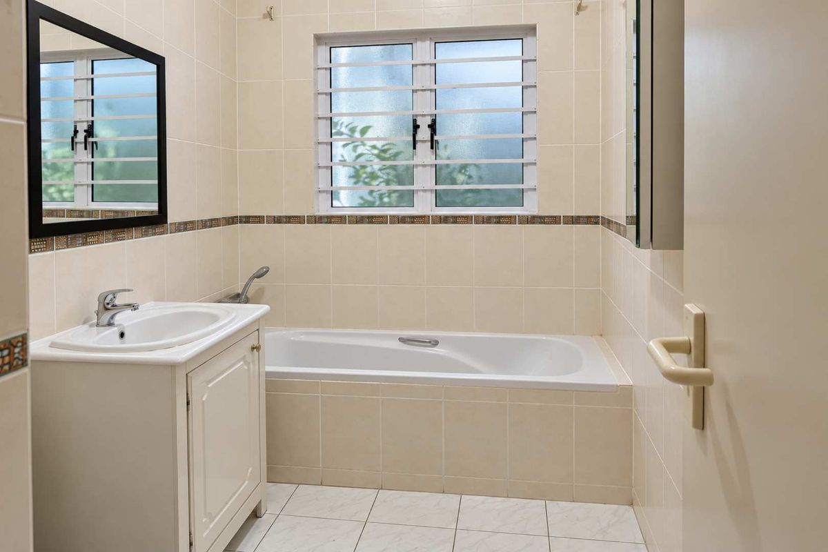 A clean, functional bathroom featuring a built-in vanity with a ceramic basin, a bathtub, and neutral wall and floor tiling.