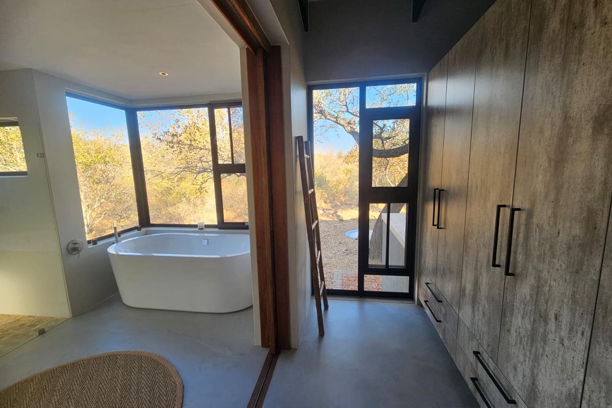 Modern bathroom featuring a freestanding soaking tub, large windows with natural views, and extensive built-in cabinetry with a contemporary finish.