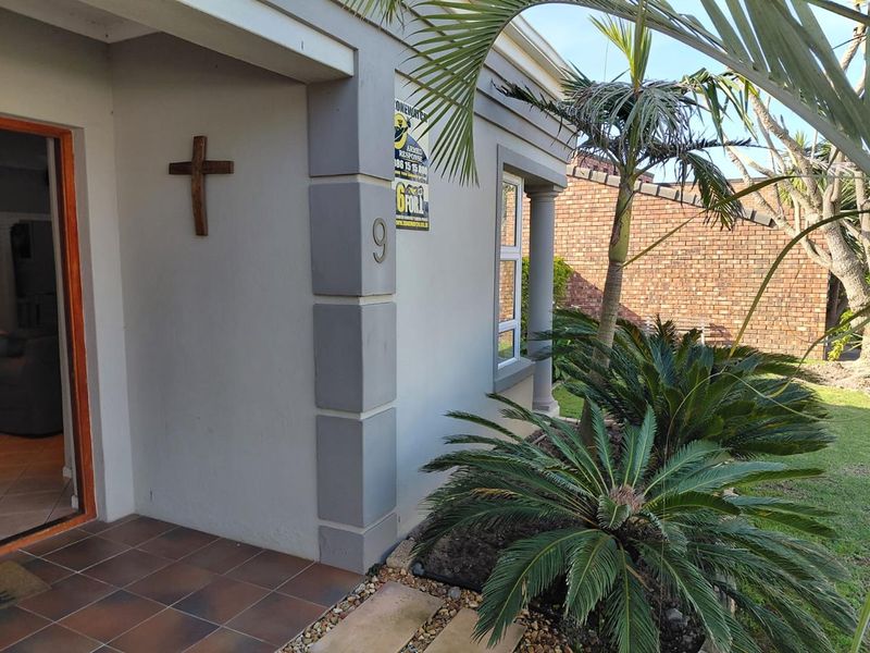 Front entrance area of the house featuring a tiled porch, concrete columns, and established garden landscaping.