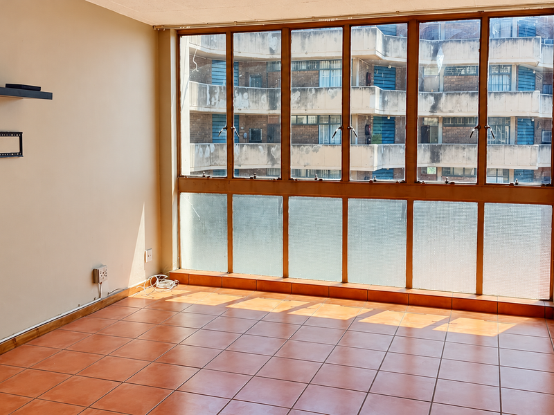 A bright, empty living area featuring large windows with natural light and durable tiled flooring, offering a blank canvas for personalization.