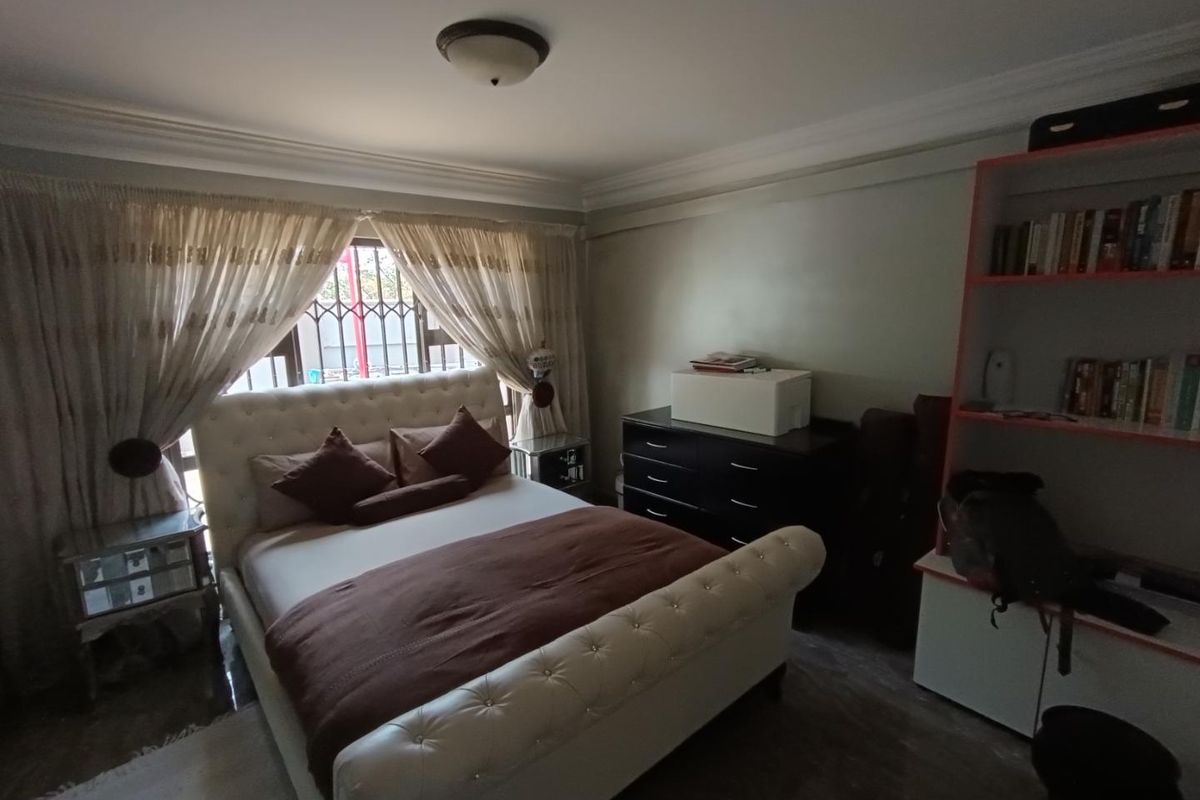 A well-lit bedroom featuring crown molding, tiled flooring, and a large window with security bars, providing a comfortable and functional living space.