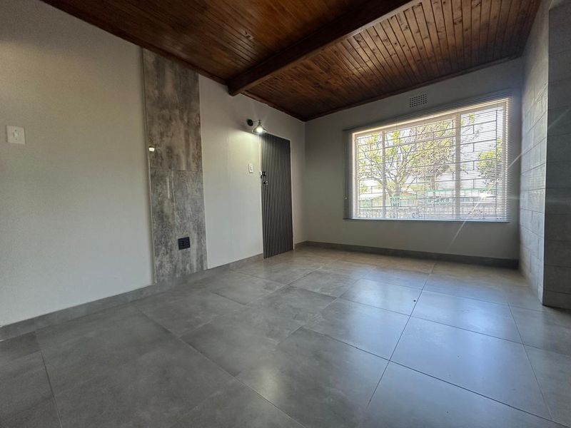 A bright, empty living room featuring a warm timber-clad ceiling with exposed beams, large format grey floor tiles, and a modern feature wall.