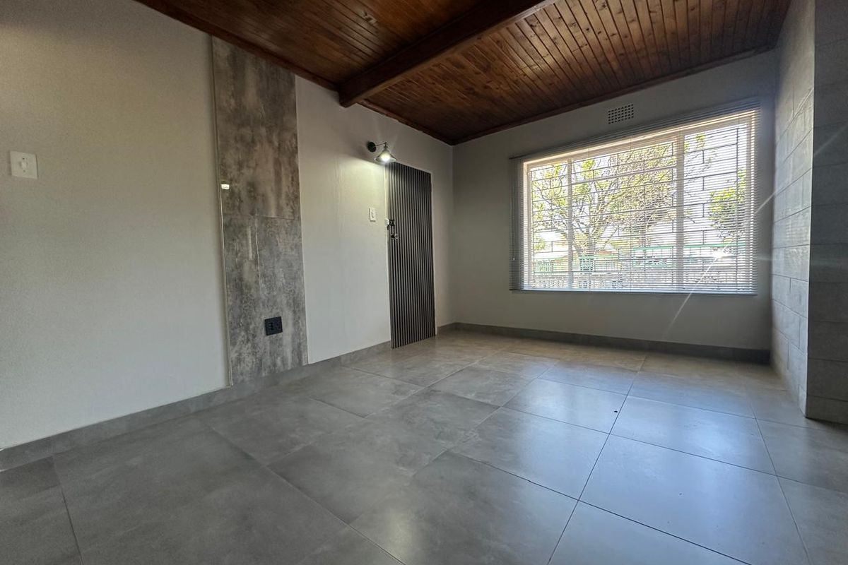 A bright, empty living room featuring a warm timber-clad ceiling with exposed beams, large format grey floor tiles, and a modern feature wall.