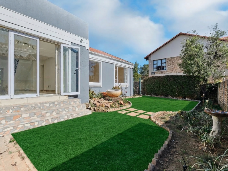 Rear exterior view featuring a landscaped garden with artificial lawn, stone-clad steps, and bi-fold doors leading into the home.