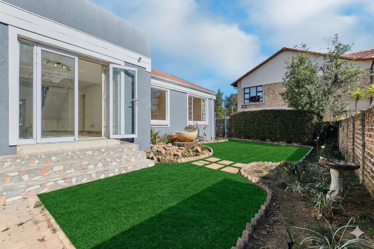 Rear exterior view featuring a landscaped garden with artificial lawn, stone-clad steps, and bi-fold doors leading into the home.