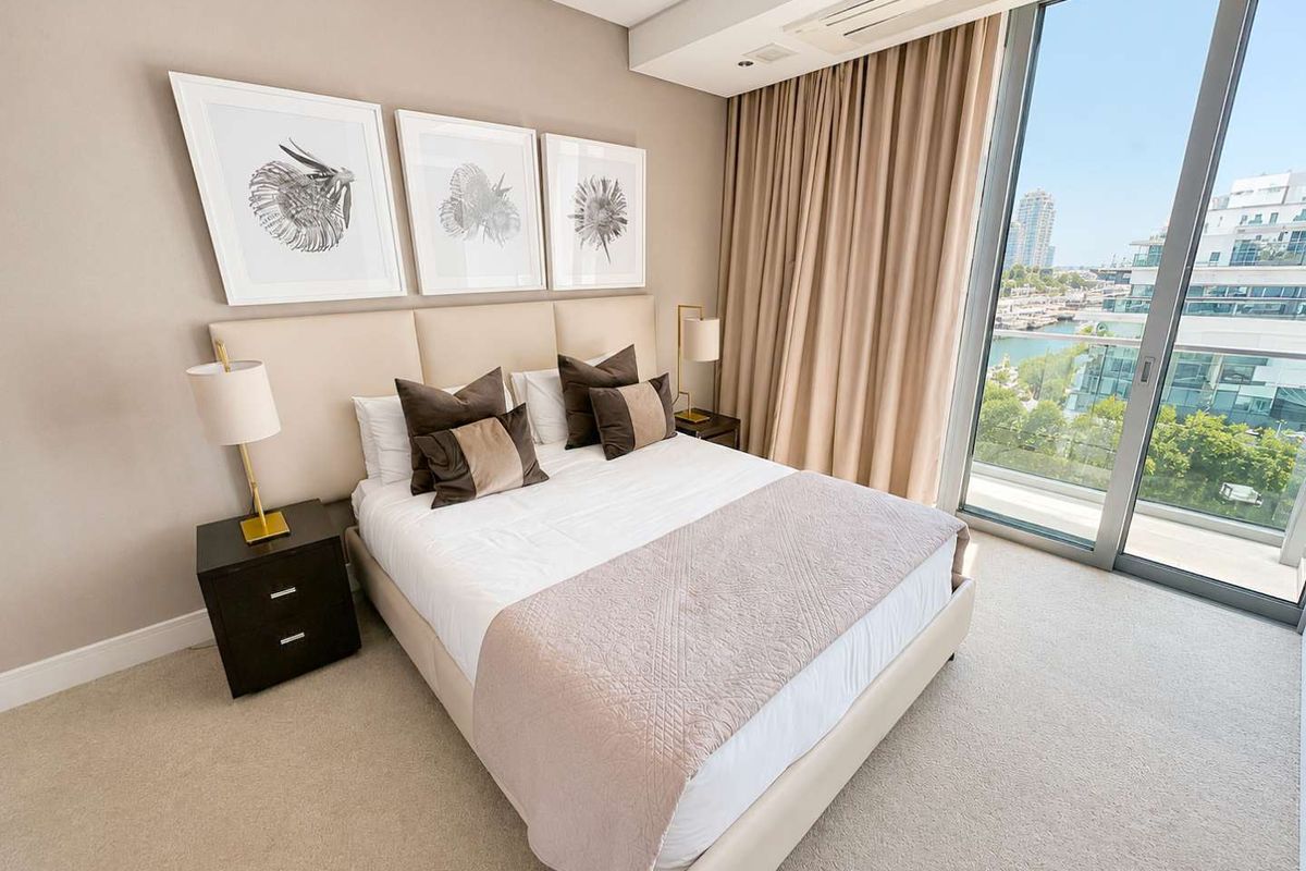 A well-appointed bedroom featuring floor-to-ceiling windows with integrated ducted air conditioning and access to a private balcony with marina views.