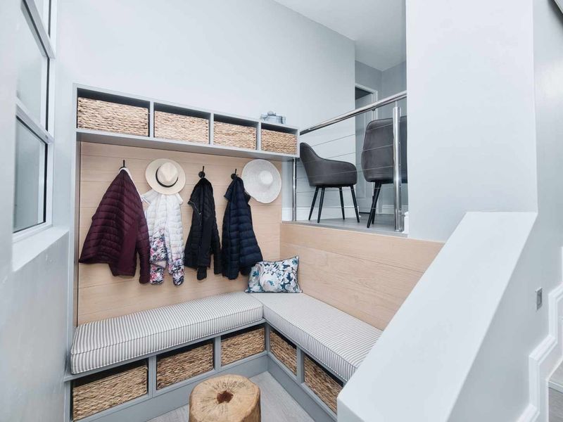 A well-designed entryway featuring custom built-in bench seating with integrated storage, overhead shelving, and a modern stainless steel balustrade.