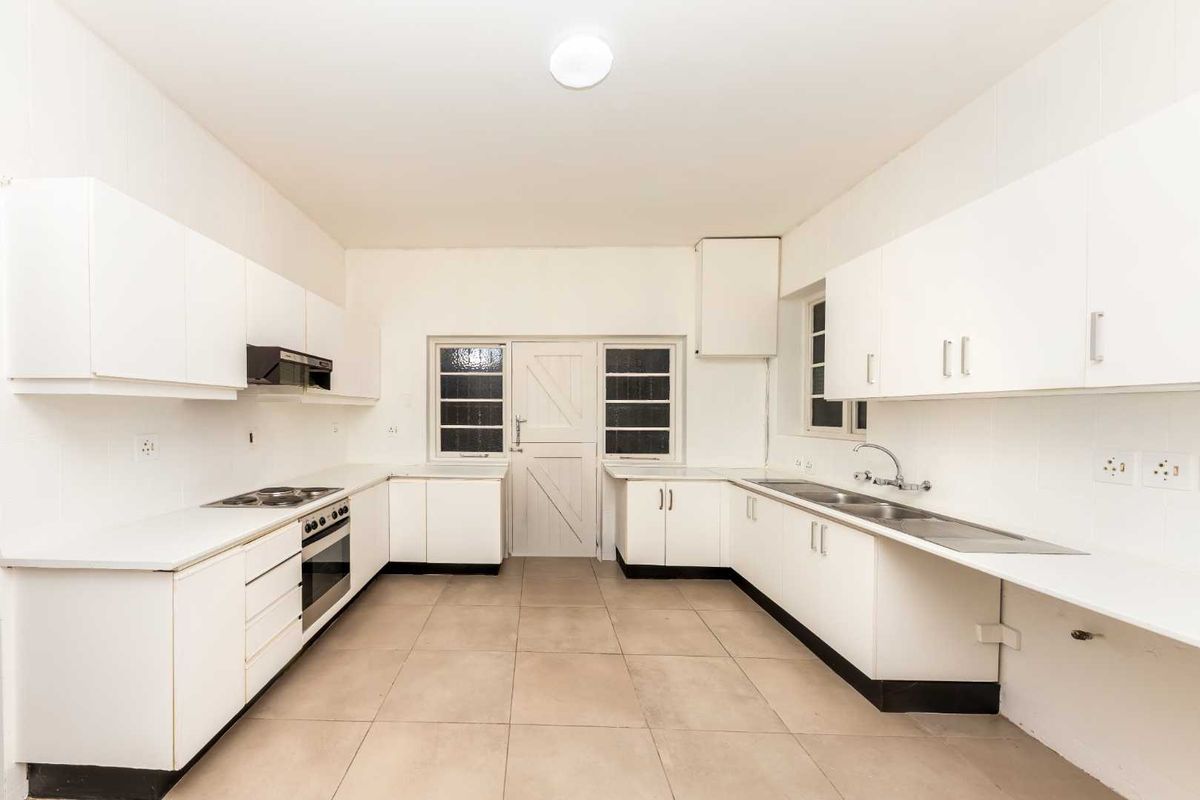 A spacious, empty kitchen featuring white cabinetry, integrated appliances, tiled flooring, and a classic stable door leading to the exterior.