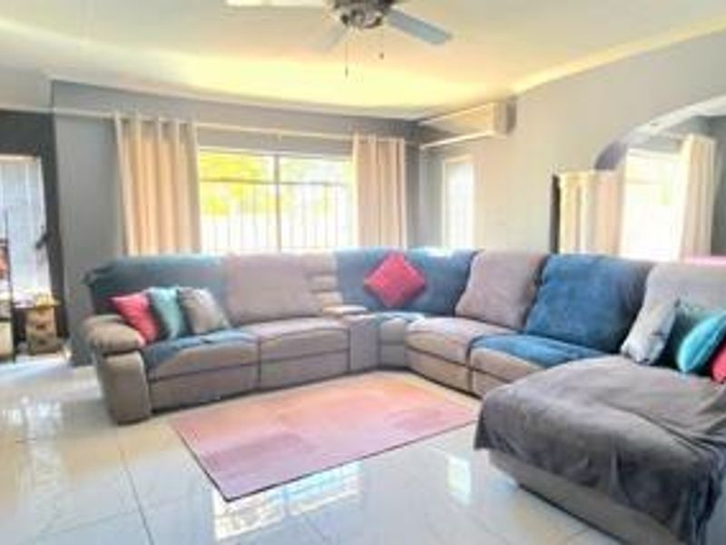 A spacious living room featuring tiled flooring, a ceiling fan, and a wall-mounted split-system air conditioner, finished with decorative cornicing.