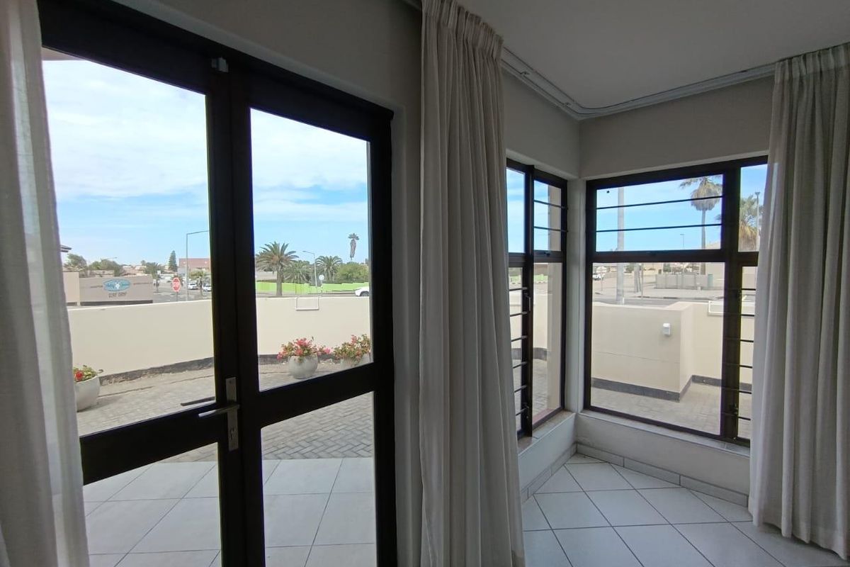 A bright living area featuring large windows and a glass door leading to an outdoor patio space with tiled flooring.