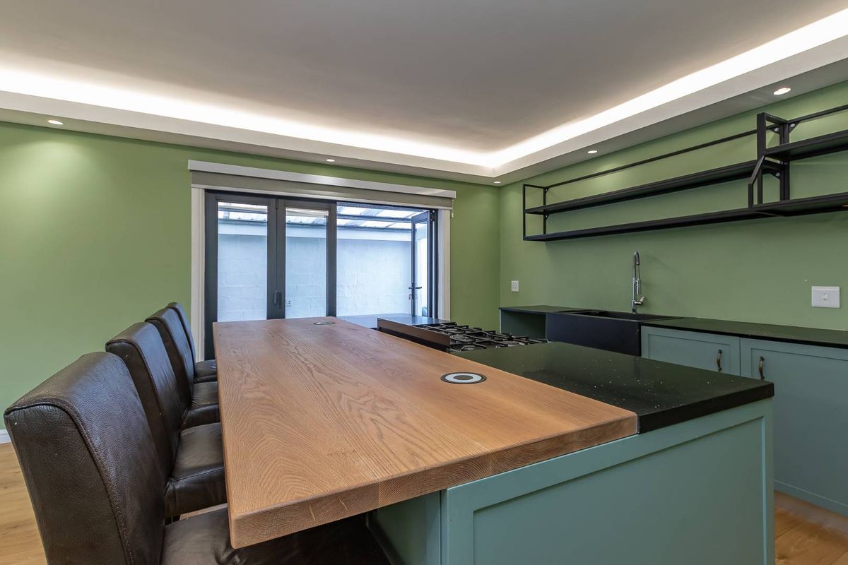 Modern kitchen featuring a large central island with a wooden breakfast bar, integrated gas hob, black stone countertops, and sleek open shelving.