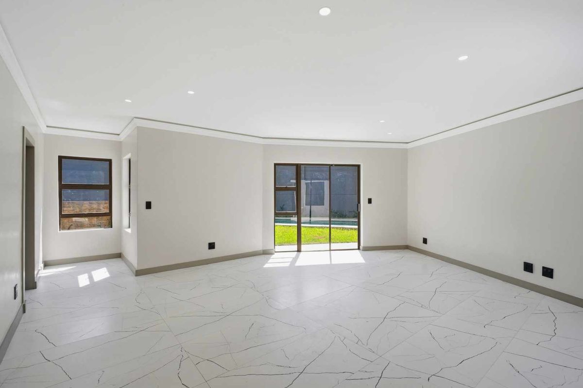 A bright, modern living area featuring large-format marble-look floor tiles, recessed ceiling lighting, and sliding glass doors leading to the garden.