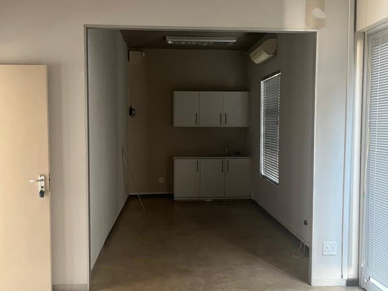 An empty office space featuring polished concrete floors, exposed ceiling, and a small kitchenette area with built-in cabinetry and a sink.