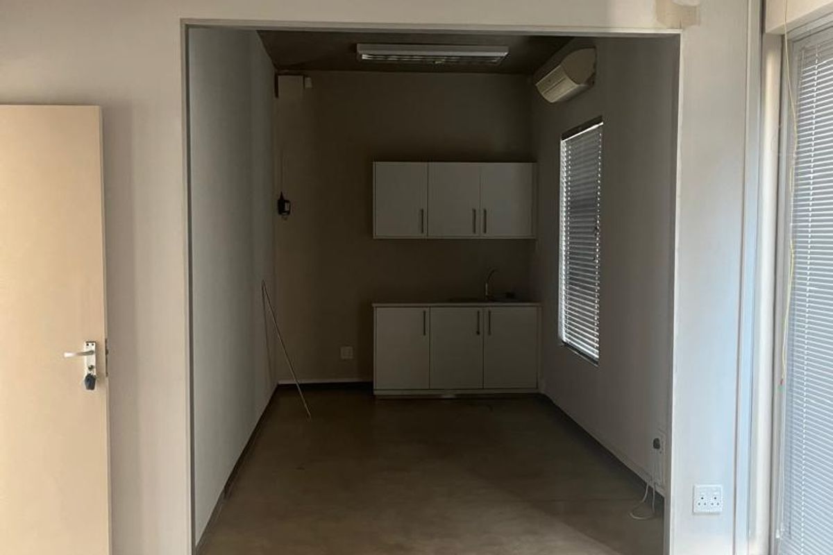 An empty office space featuring polished concrete floors, exposed ceiling, and a small kitchenette area with built-in cabinetry and a sink.