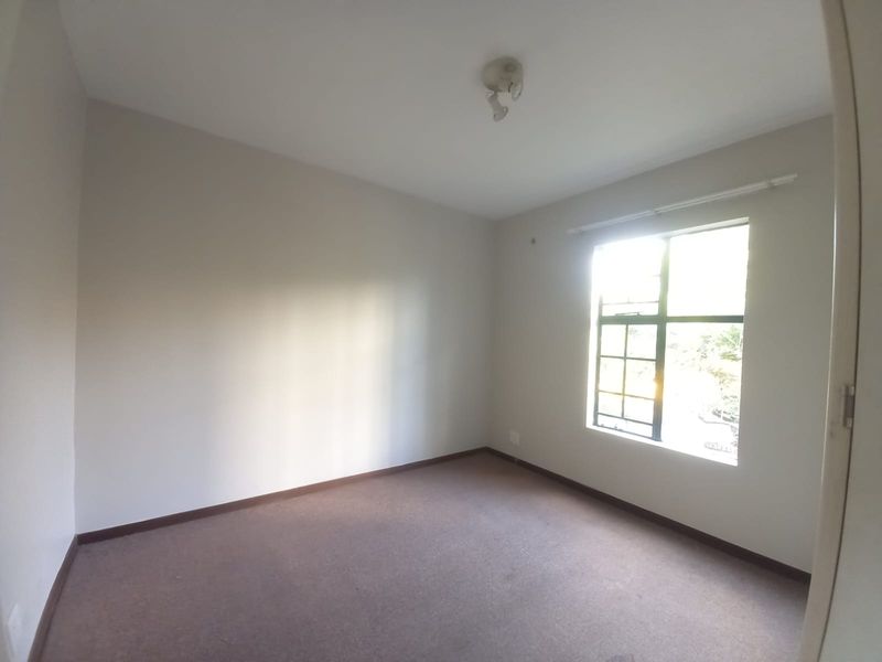 An empty bedroom featuring neutral walls, carpeted flooring, and a window allowing natural light.
