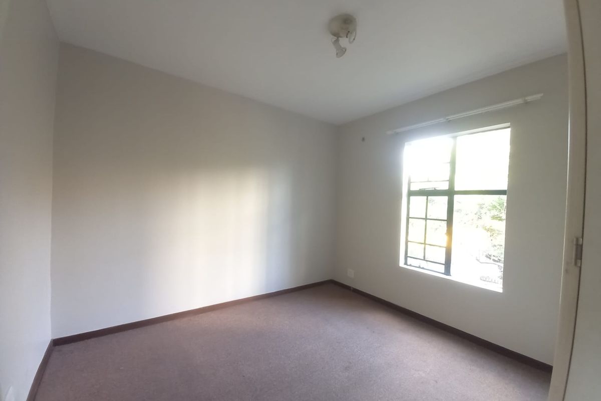 An empty bedroom featuring neutral walls, carpeted flooring, and a window allowing natural light.