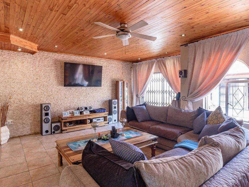 Spacious living room featuring a warm timber-clad ceiling, stone-cladding feature wall, tiled flooring, and large windows with security gates.