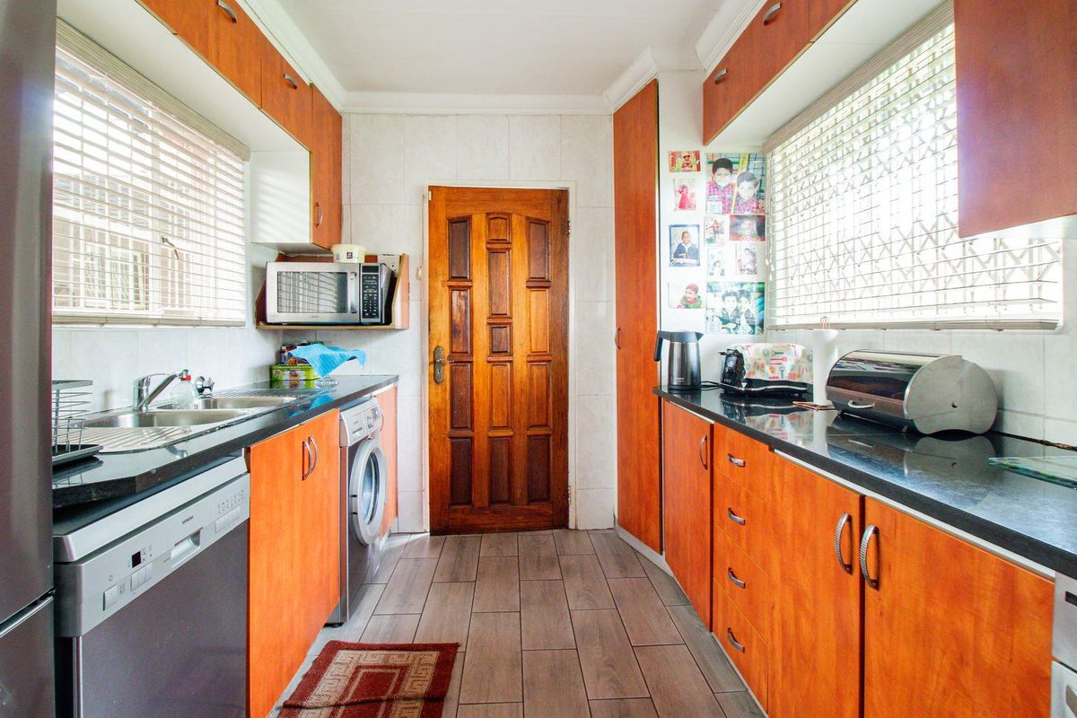 A functional galley-style kitchen featuring wood-finish cabinetry, dark countertops, tiled flooring, and integrated appliance spaces.