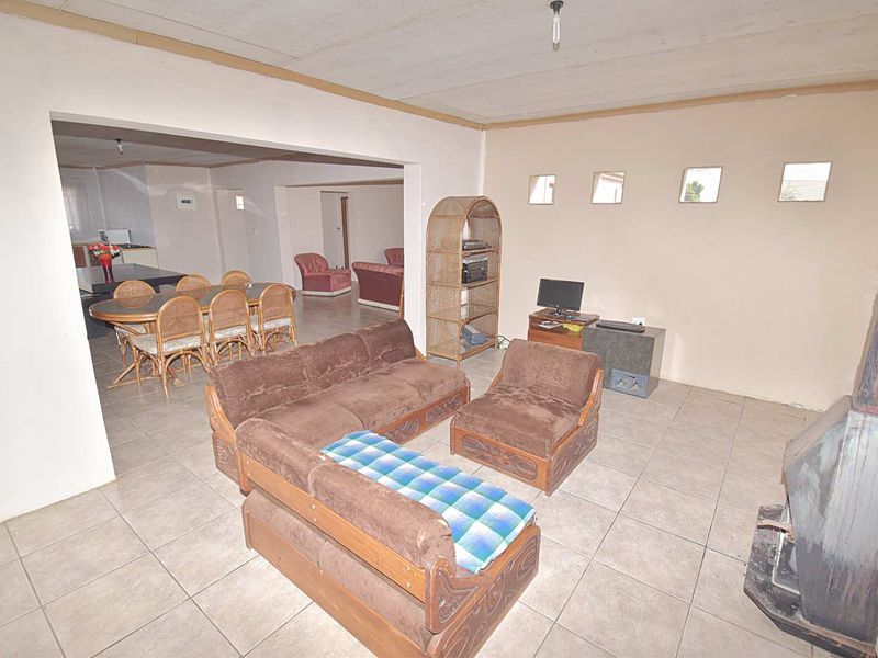 Open-plan living and dining area featuring tiled flooring, a freestanding fireplace, and clerestory windows, offering a spacious layout with potential for modernization.