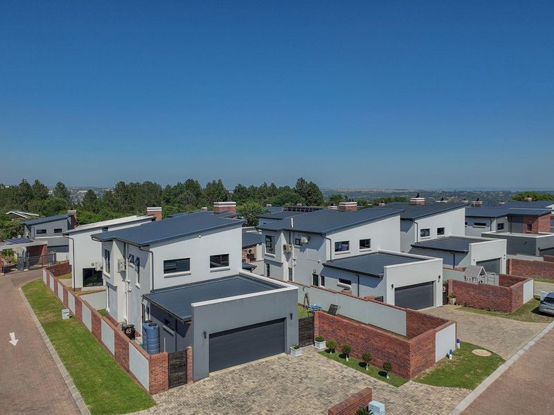 Aerial view of a modern residential estate featuring contemporary homes with pitched metal roofs, paved driveways, and brick boundary walls.