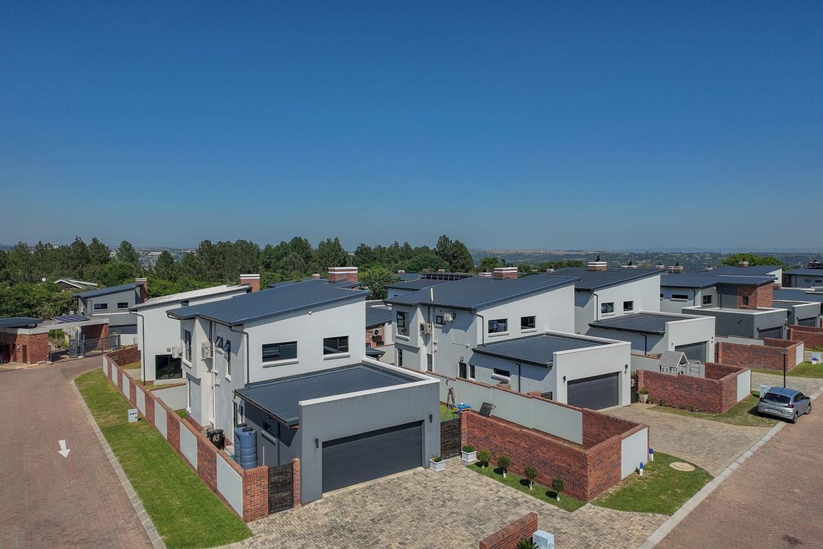 Aerial view of a modern residential estate featuring contemporary homes with pitched metal roofs, paved driveways, and brick boundary walls.