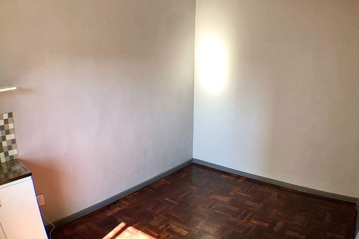 An empty kitchen area featuring dark parquet flooring, mosaic tile backsplash, and basic cabinetry, awaiting a modern update to enhance its functionality and appeal.
