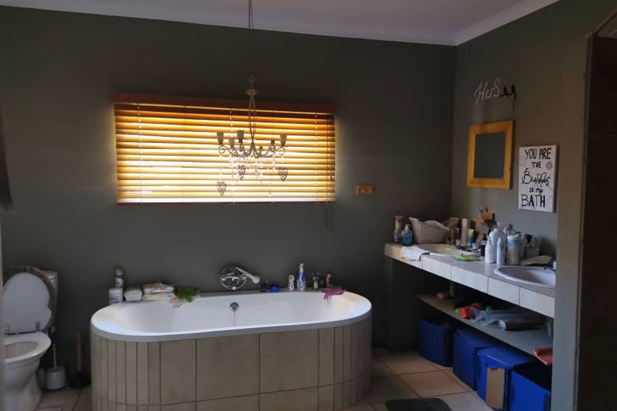 A spacious bathroom featuring a built-in tiled bathtub, dual vanity with tiled countertop, and wooden blinds.