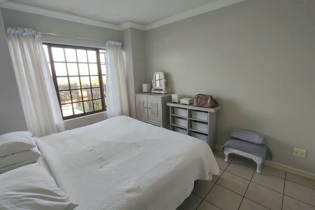 A well-lit bedroom featuring neutral wall tones, tiled flooring, crown molding, and a large grid-pattern window providing natural light.