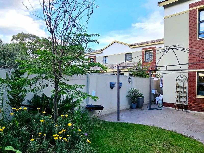 A private rear garden featuring a paved patio area, a metal gazebo frame, and established landscaping against a brick and plaster townhouse facade.
