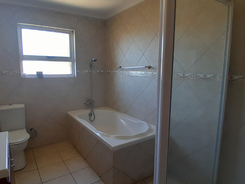 A functional bathroom featuring a built-in bathtub, separate shower enclosure, toilet, and vanity basin with neutral wall and floor tiling.