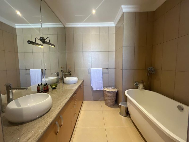 Modern bathroom featuring a double vanity with stone countertop, vessel sinks, a freestanding bathtub, and full-height wall tiling with recessed lighting.