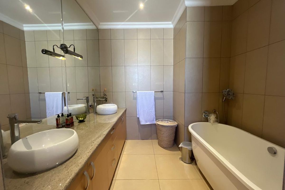 Modern bathroom featuring a double vanity with stone countertop, vessel sinks, a freestanding bathtub, and full-height wall tiling with recessed lighting.