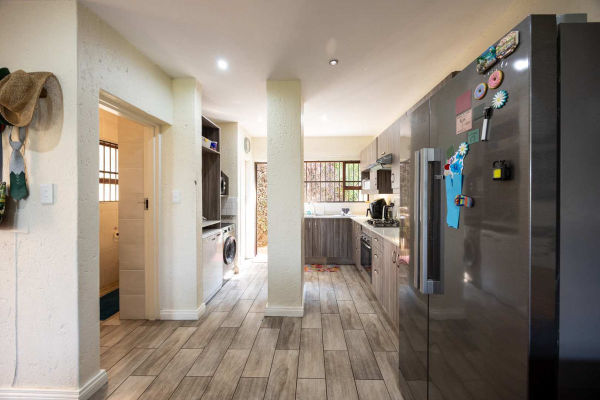 A functional kitchen featuring modern wood-look cabinetry, integrated appliances, and durable laminate flooring, with a separate laundry area accessible through the hallway.